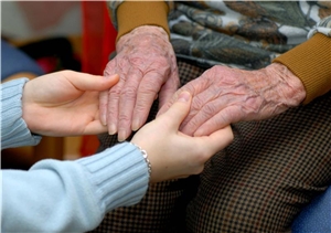 Die Hände einer Mitarbeiterin halten die Hände einer Bewohnerin in einer Altenpflegeeinrichtung.