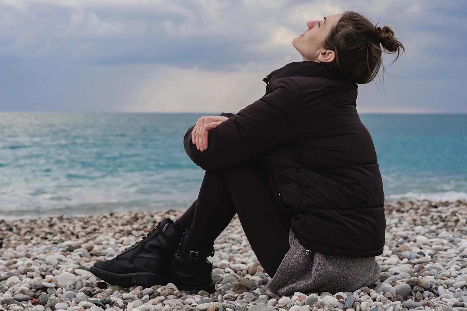 Eine junge Frau sitzt an einem Kieselsteinstrand am Meer.