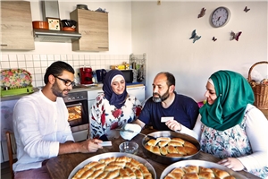 Ehrenamtlicher und Flüchtlingsfamilie beim Essen Vier Personen sitzen am Esstisch.