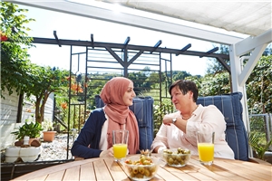 Zwei Frauen sitzen am Tisch und unterhalten sich, eine tr�gt ein Kopftuch.
