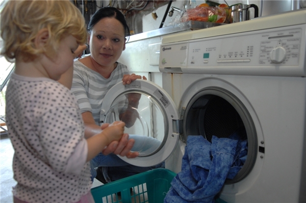 junge Mutter mit Kleinkind am Wäsche waschen