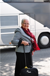 Seniorin steht mit Rollkoffer vor Reisebus