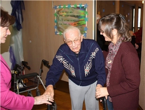 Zwei Mitarbeiterinnen helfen einem gehbehinderten Bewohner im Caritas-Altenzentrum St. Ulrich in Neustadt.