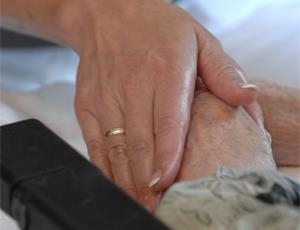 Die Hand einer Mitarbeiterin umfasst die Hand einer Bewohnerin eines Altenheims. 