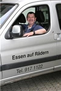 Ein Mitarbeiter sitzt im Auto mit der Aufschrift 'Essen auf Rädern'. Essen auf Rädern hoch