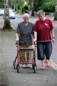 Kurzzeitpflege Eine Mitarbeiterin begleitet eine Bewohnerin eines Caritas-Altenzentrums bei einem Spaziergang. Die Dame ist auf einen Rollator angewiesen.