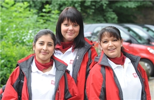Drei junge Frauen in weiß-roter Arbeitskleidung der Caritas. Drei junge Frauen in weiß-roter Arbeitskleidung der Caritas.