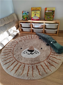 Tagespflege Julia Hahn in Wald-Michelbach Foto eines Kinderzimmers, darin ein runder Teppich mit Löwengesicht, ein Stoffkrokodil und ein Regal mit Kinderbüchern und Spielsachen