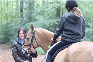 Lernhelferin Marla blickt in die Kamera, Schülerin Sophie sitzt auf dem Pferd