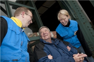 Zwei ehrenamtliche Helferinnen und Helfer mit einem Rollstuhlfahrer am Bahnhof