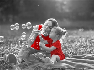 Mutter sitzt mit der kleinen Tochter beim Seifenblasenpusten auf der Piknikdecke. In Graustufen, rot illustrierte Kleider. (c) Ljiljana | www.stock.adobe.com | Nachbearbeitung Caritas FRG.