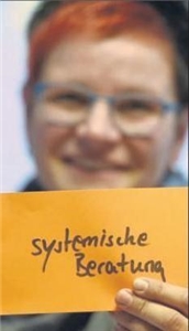 Frau zeigt einen orangen Zettel mit dem Begriff "systemische Beratung"