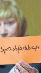 Frau zeigt einen orangen Zettel mit dem Wort "Sprachfachkraft"