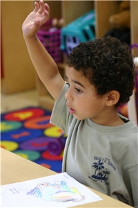 Stiftungsflyer Foto eines Migrantenjungen Ein junge mit Migrationshintergrund von etwa 6 Jahren hebt in der Schule die Hand