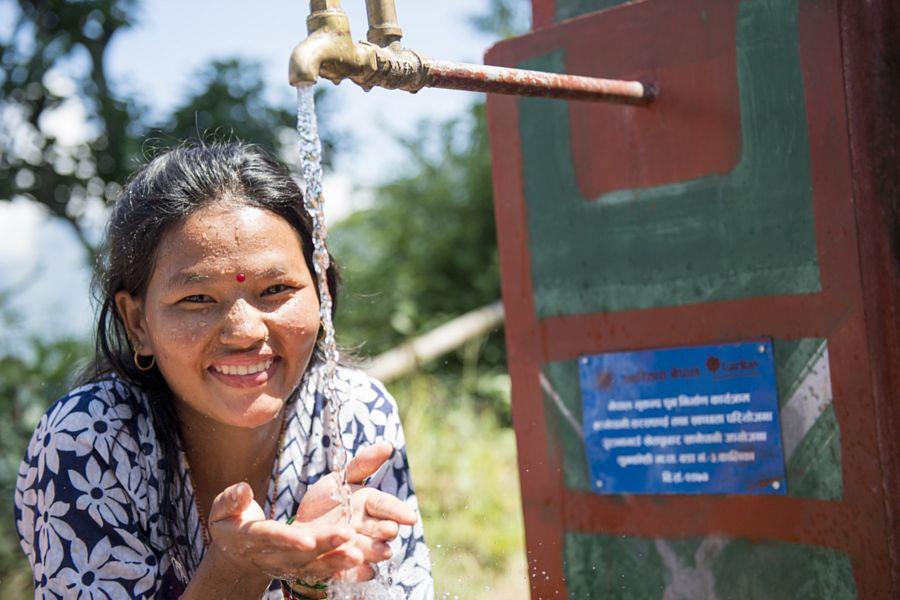 Frau am Brunnen hält Hände unter den Wasserstrahl und lacht