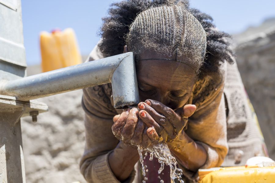 Frau trinkt klares Wasser an einem Brunnen