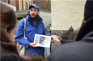 Mann erklärt einer Gruppe von Jugendlichen etwas, im Hintergrund das Modell einer Synagoge.