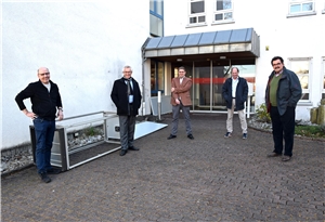 Fünf Männer stehen mit Abstand zueinander vor dem Eingang einer Einrichtung.