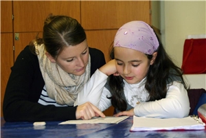 Eine junge Frau hilft einem Mädchen bei den Hausaufgaben.