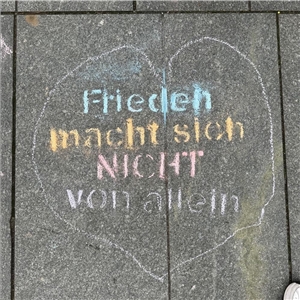Ein Herz mit Kreide auf die Straße gemalt. Darin steht mit bunten Farben: Frieden macht sich nicht von allein.