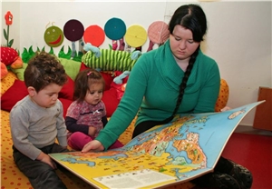 Eine Frau zeigt zwei Kindern ein Buch.