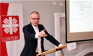 Das Foto zeigt einen Redner an einem Pult und daneben eine Präsentation auf Leinwand.