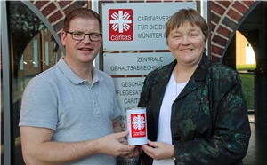 Ein Mann und eine Frau halten zusammen eine Spendendose der Caritas in der Hand.