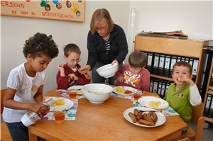 Das Foto zeigt eine Gruppe von Kindern im Kindergarten um einen mit Essen gedeckten Tisch.