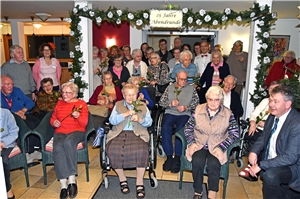 Eine große Gruppe älterer Menschen sitzen und stehen fröhlich zusammen. 