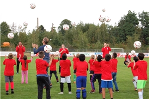 Das Foto zeigt eine Gruppe an Jungen in Sportkleidung auf einem Fußballplatz, die Bälle in die Luft werfen.