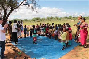 In der Savanne, in dem Schatten eines Baumes spielen Massai-Kinder auf einem blauen Tuch.