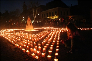 Das Foto zeigt viele brennende Kerzen auf einem Platz und ein Mädchen, das am Rand eine der Kerzen anzündet.