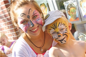Eine junge Frau hat einen Schmetterling ins Gesicht gemalt. Rechts neben ihr ist ein Junge der ein tigerartiges Make-Up hat.