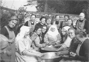 Das historische Schwarz-weiß-Foto zeigt eine Runde von Menschen mit Ordensschwestern beim Kartoffelschälen.