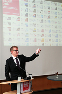 Das Bild zeigt einen Referenten vor einer Projektion mit vielen kleinen Logos