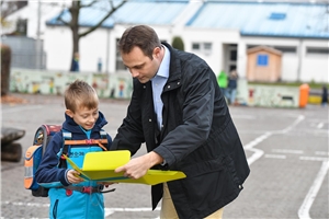 Das Foto zeigt einen Vater mit seinem Sohn vor einer Schule.