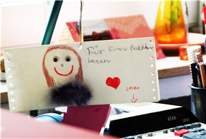 Das Foto zeigt einen mit einem Gesicht und einem roten Herzen bemalten Zettel auf einem Schreibtisch.