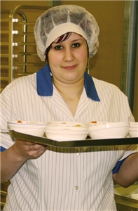 Mitarbeiterin Melissa Zacher steht mit einem Tablett voller Schälchen in der Großküche des Studentenwerks Essen-Duisburg