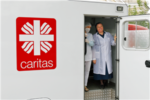 Ein weißer Ambulanzbus der Caritas Omsk mit großem Caritas-Logo. In der geöffneten Tür stehen zwei Mitarbeiterinnen und blicken hinaus