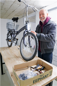 Ralf Tilke steht vor einem auf einem Tisch stehenden Fahrrad in einer Fahrradwerkstatt, die sich im Keller eines Wohnhauses befindet. Neben dem Fahrrad liegt Werkzeug in einer Kiste.