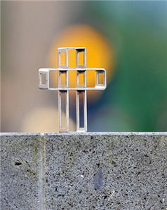 Ein kleines Stahlkreuz, das eine verkleinerte Nachbildung des von Benediktinerpater Abraham Fischer geschaffenen Kreuzes darstellt, dass auf einer Mauer steht