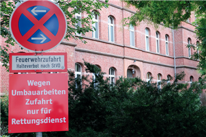 Ein absolutes Halteverbotsschild (Feuerwehrzufahrt) mit einem roten Hinweisschild. Im Hintergrund sind eine Hecke und das Marienhospital in Brühl zu sehen.Hintergrund