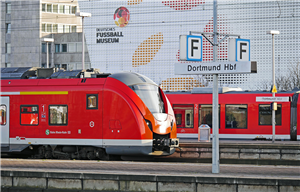Zwei Bahnsteige des Hauptbahnhofs in Dortmund, an denen zwei Regionalbahnen stehen. Im Hintergrund ist das 'Deutsche Fußball Museum' zu sehen.