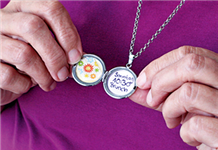 Ein aufgeklapptes Amulett, was um den Hals einer Seniorin hängt, und ein Bild mit Blumen und einen Terminhinweis enthält