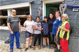 Eine Familie aus Solingen-Unterburg, die mit der Caritas Mitarbeiterin Silvia Hamacher vor einem zerstörtem Haus steht