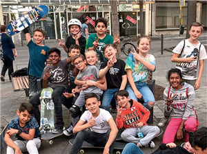 Eine große Gruppe von Mädchen und Jungen mit Skateboards sitzen auf einem Platz im Stadtteil Mönchengladbach-Rheydt zusammen