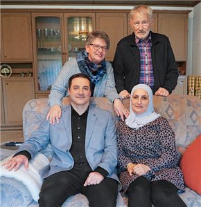 Basel und Ramia Al Shoueb sitzen in einem Wohnzimmer auf einem Sofa. Dahinter stehen die Ehrenamtlichen Annegret und Bernd Stöcker.