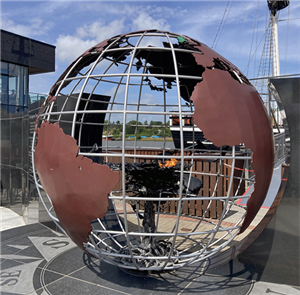 Eine hohle Weltkugel aus Stahl mit rostbrauner Landmasse und einer brennenden Fackel im inneren als Gedenkstätte