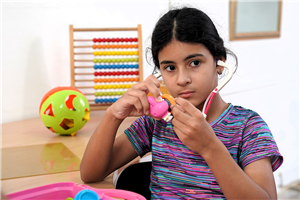 Ein kubanisches Mädchen, dass mit einem Spielzeug-Stethoskop spielt. Im Hintergrund liegt weiteres Spielzeug.