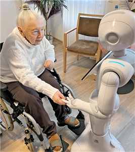 Eine im Rollstuhl sitzende Seniorin gibt dem Roboter Pepper die Hand
